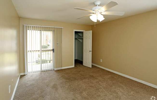 an empty living room with a ceiling fan and a door to a balcony