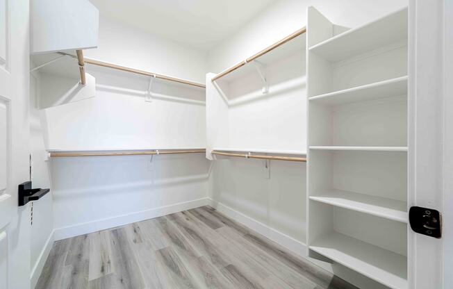 a walk in closet with white walls and wooden floors