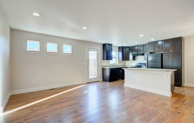 an empty living room and kitchen with wood flooring and black cabinets at Copper Pines, Bozeman, Montana