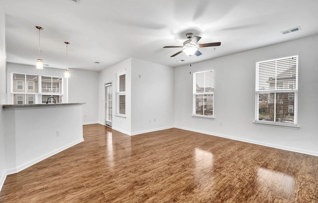 an empty living room with a ceiling fan and a kitchen