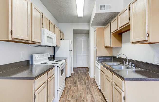 A kitchen with wooden cabinets and white appliances at Saxony at Chase Oaks Apartments in Dallas, TX.