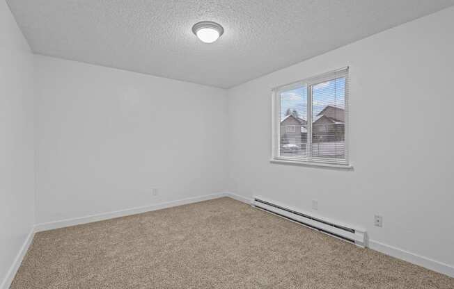 A room with a carpeted floor and a window showing a view of houses outside.