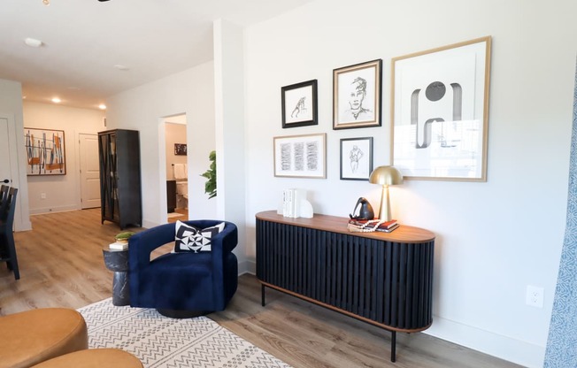 a living room with a blue chair and a cabinet and a white wall with pictures