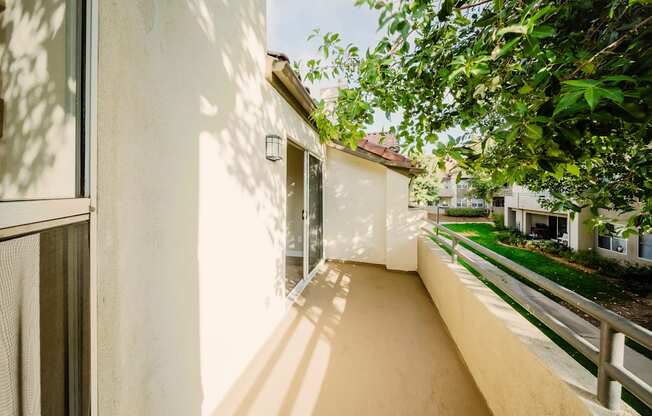 A balcony with a white wall and a railing with a view of a green lawn and a house.