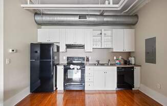 A black refrigerator is in a kitchen with white cabinets.