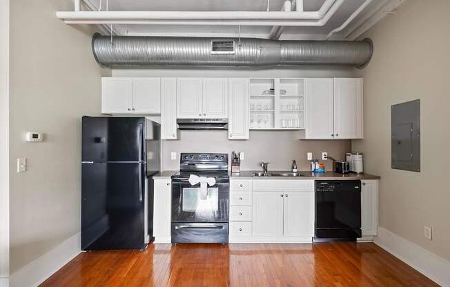 A black refrigerator is in a kitchen with white cabinets.