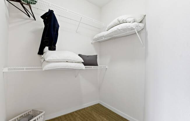 a room with a white wall and a white shelf with white pillows and a black jacket
