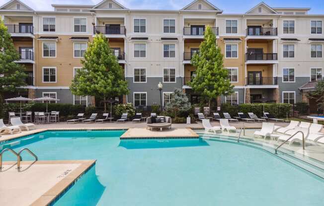 a swimming pool with lounge chairs and a fire pit in front of an apartment building