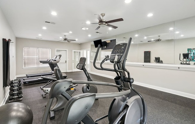 A spacious gym with treadmills, elliptical machines, and a mirrored wall.