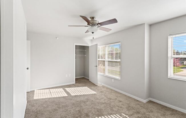 a spacious room with carpet, a ceiling fan, and ample natural light from large windows