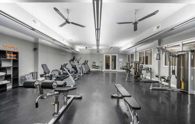 Fully-equipped gym at West 39th Street Apartments with workout benches, cable machines, cardio stations, and ceiling fans.
