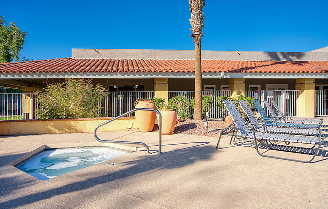 A pool area with a hot tub, chairs, and a palm tree.