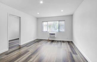 a living room with white walls and wooden floors and a window