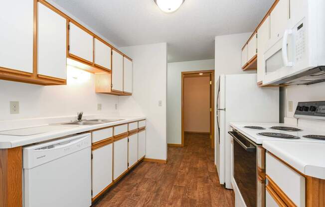 a kitchen with white appliances and wood flooring and white cabinets. Anoka, MN Dellwood Estates