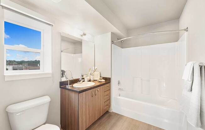 A white bathroom with a large window and a wooden vanity.