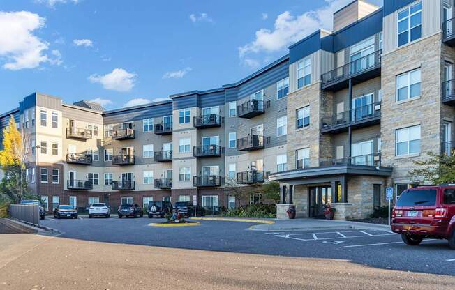 A row of apartment buildings with cars parked in front.