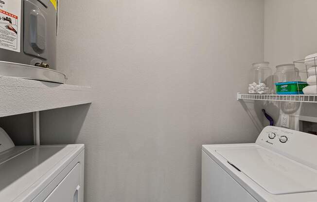 A white washing machine sits in a laundry room with a shelf above it.