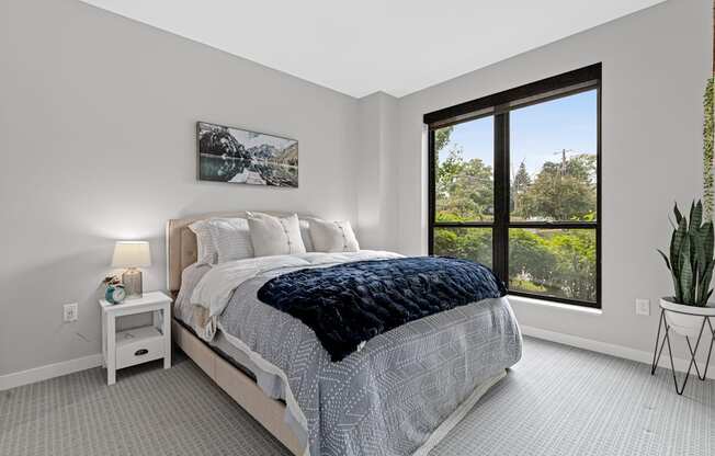 A bedroom with a large bed and a window overlooking a tree-filled landscape.