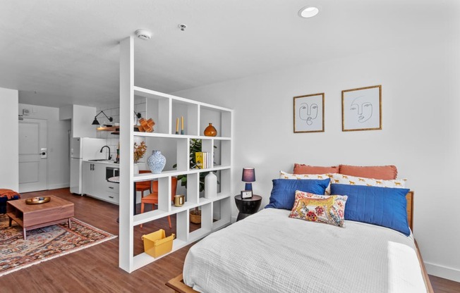 a bedroom with white walls and a white bed with blue and orange pillows