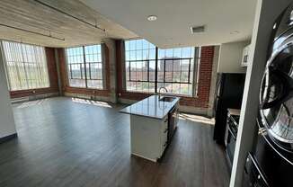 an empty living room with a kitchen and large windows