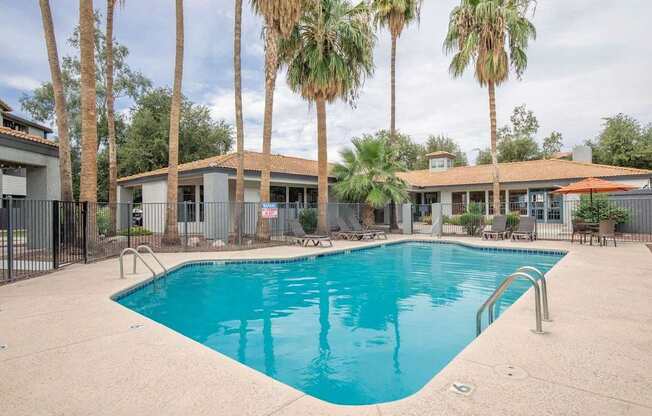 A swimming pool surrounded by palm trees and a building in the background.