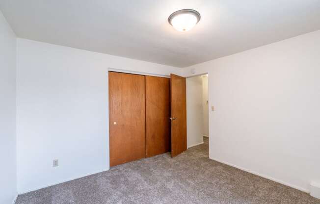 a room with a carpeted floor and a door to a closet. Fargo, ND Spring Apartments