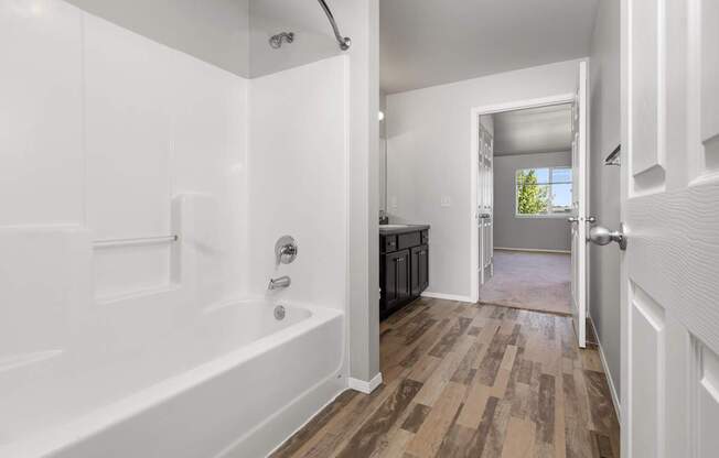 A white bathroom with a wooden floor and a white tub.