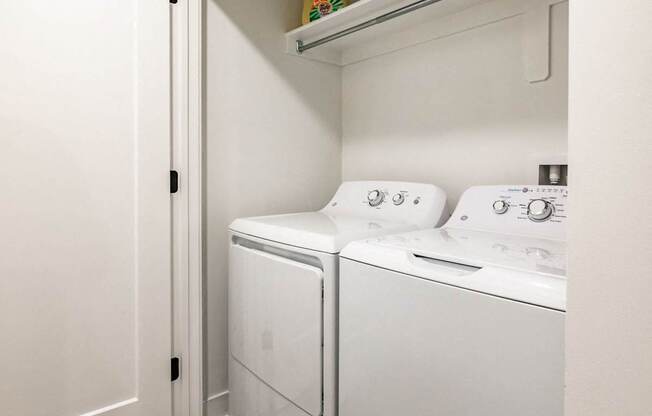 a washer and dryer in a white laundry room with a shelf above it