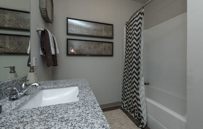A bathroom with a granite counter top and a shower with a black and white curtain.