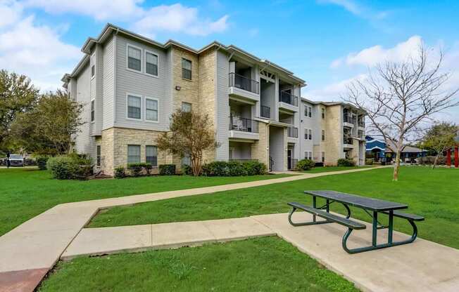 A large apartment complex with a green lawn and a picnic table in front.