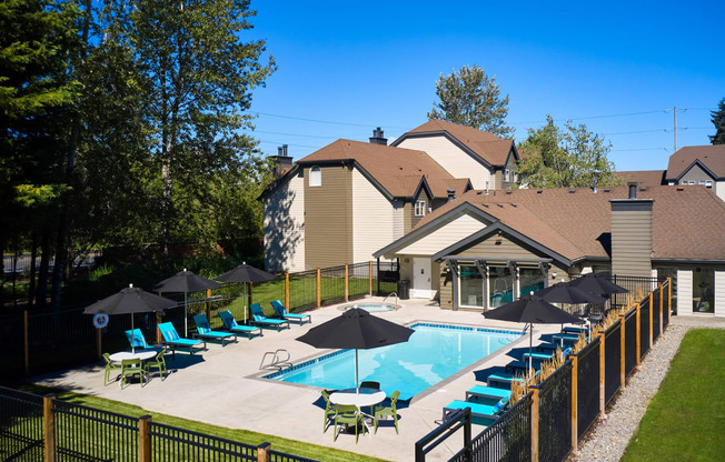 a swimming pool with lounge chairs and umbrellas in front of a house