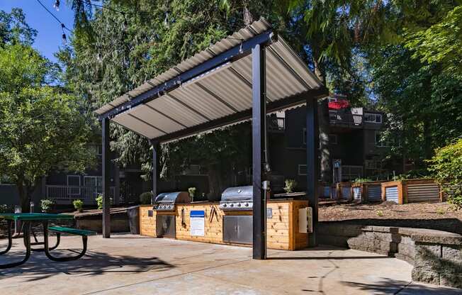 A covered picnic area with a grill and a table.