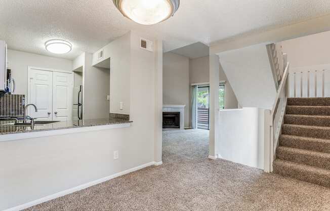 a living room with a staircase and a kitchen in the background