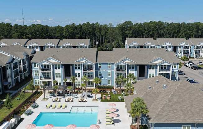 A large apartment complex with a pool and a patio with chairs and umbrellas.