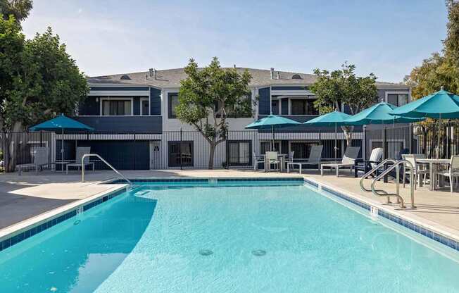 A swimming pool with a blue umbrella and a building in the background.