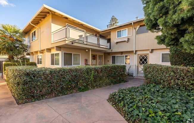 a house with a sidewalk and a hedge in front of it