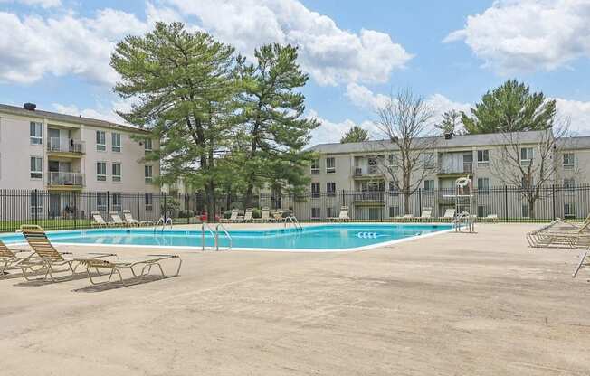 A pool surrounded by chairs and trees in front of apartment buildings.