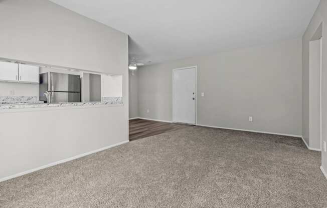 the living room and kitchen of an apartment with white walls and a carpeted floor