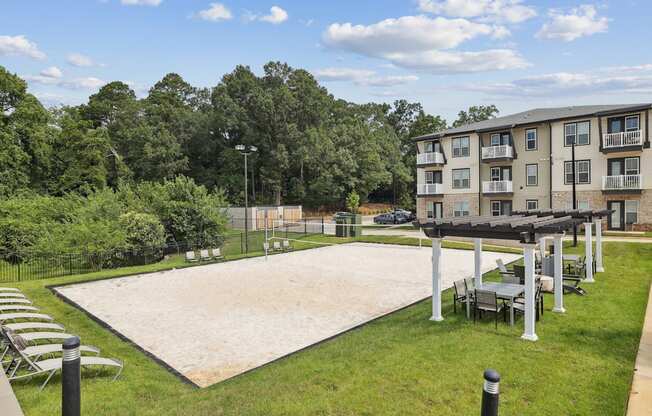 A large sand volleyball court is surrounded by trees and apartment buildings.
