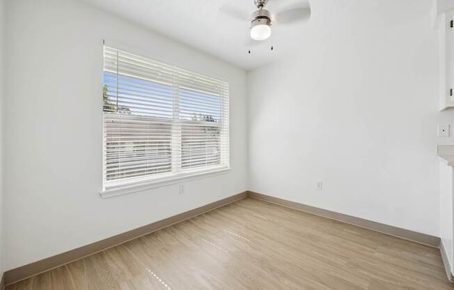 A room with a window covered by white blinds and a ceiling fan.