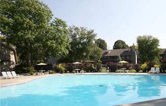 A swimming pool with trees and a house in the background at Eden West Apartments.