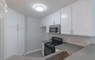 an empty kitchen with white cabinets and a stove and microwave at Warner Center Townhomes, California, 91303