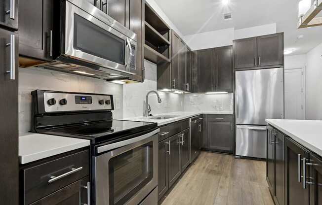 A modern kitchen with stainless steel appliances, dark cabinets, and wooden floors at Knox Heights Apartments in Dallas, TX