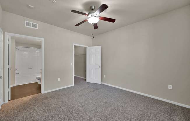 a bedroom with a ceiling fan and a door to a bathroom