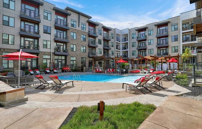 a swimming pool with chaise lounge chairs and umbrellas in front of an apartment building