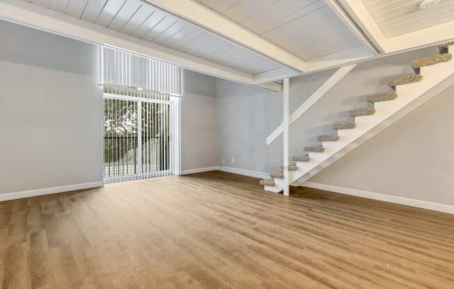 an empty living room with stairs and a door to a balcony