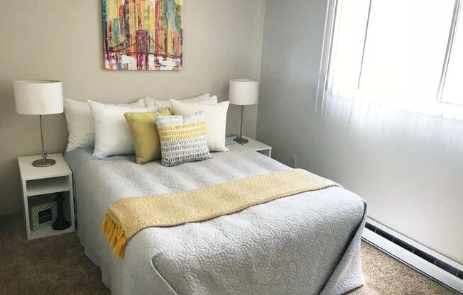 Bedroom with queen sized bed and large window with blinds. Staged with bed, side table, lamp and wall art.at The Lakes Apartments, Moses Lake, 98837