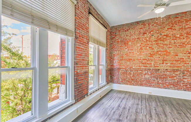 an empty room with large windows and a red brick wall