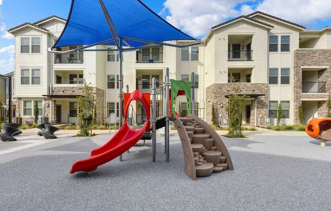 Outdoor playground, Red Slide,  and blue UV sun trap over it at Morgan Ranch Apartments, California