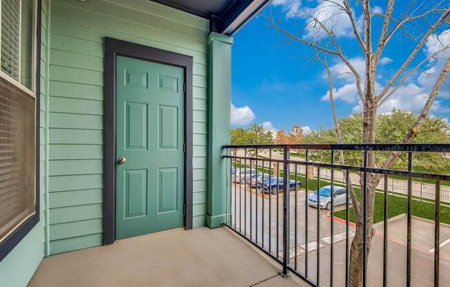 A green door is on a house with a black railing.